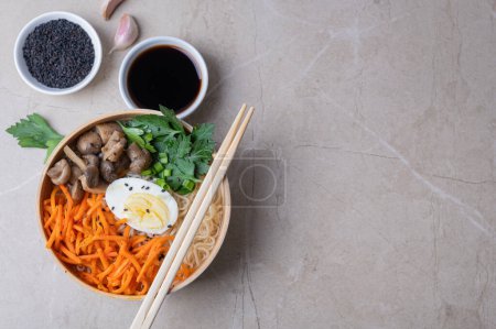 Téléchargez les photos : Soupe de nouilles, ramen dans un bol blanc (bol) avec oeuf de poulet, carottes, champignons sur un fond de pierre claire. Asiatique traditionnel fast food - en image libre de droit