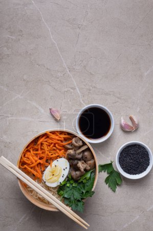 Téléchargez les photos : Soupe de nouilles, ramen dans un bol blanc (bol) avec oeuf de poulet, carottes, champignons sur un fond de pierre claire. Asiatique traditionnel fast food - en image libre de droit