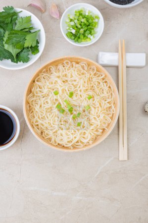 Foto de Placa de bambú blanco (bowl) con fideos de huevo y platos con ingredientes para ello sobre un fondo claro. Comida rápida tradicional asiática - Imagen libre de derechos