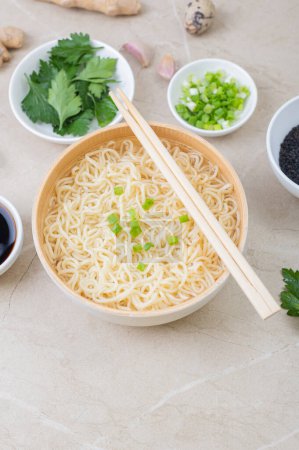 Téléchargez les photos : Assiette en bambou blanc (bol) avec nouilles aux œufs et assiettes avec ingrédients pour elle sur un fond clair. Asiatique traditionnel fast food - en image libre de droit