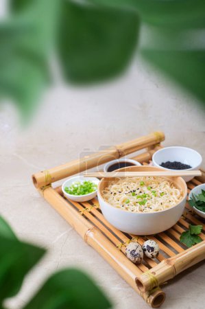 Photo for White bamboo plate (bowl) with egg noodles and plates with ingredients for it on a bamboo serving tray against a light background. Asian traditional fast food - Royalty Free Image