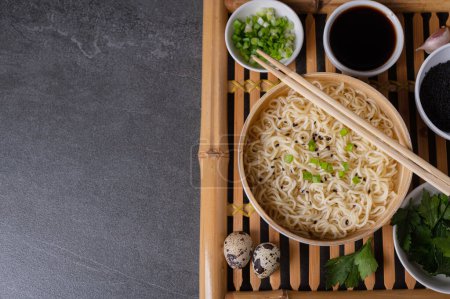 Photo for White bamboo plate (bowl) with egg noodles and plates with ingredients for it on a bamboo serving tray on a dark marble (slate) background. Asian traditional fast food - Royalty Free Image