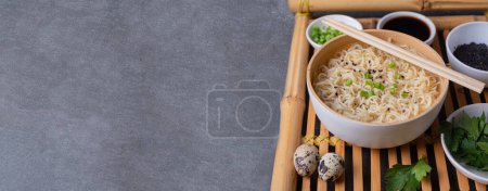 Téléchargez les photos : Assiette en bambou blanc (bol) avec nouilles aux œufs et assiettes avec ingrédients pour elle sur un plateau de service en bambou sur un fond en marbre foncé (ardoise). Asiatique traditionnel fast food - en image libre de droit