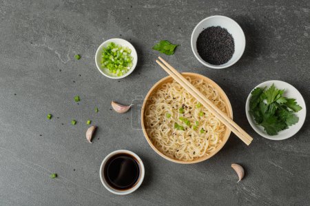 Foto de Placa de bambú blanco (bowl) con fideos de huevo y platos con ingredientes para ello sobre un fondo de mármol oscuro (pizarra). Comida rápida tradicional asiática - Imagen libre de derechos