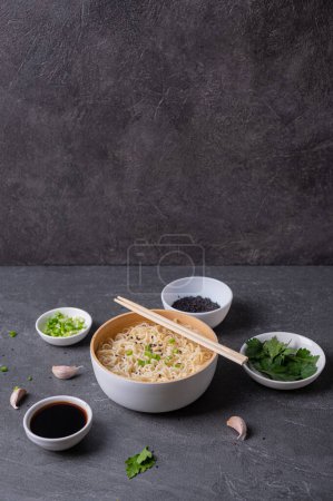 Téléchargez les photos : Assiette en bambou blanc (bol) avec nouilles aux œufs et assiettes avec ingrédients pour elle sur un fond en marbre foncé (ardoise). Asiatique traditionnel fast food - en image libre de droit