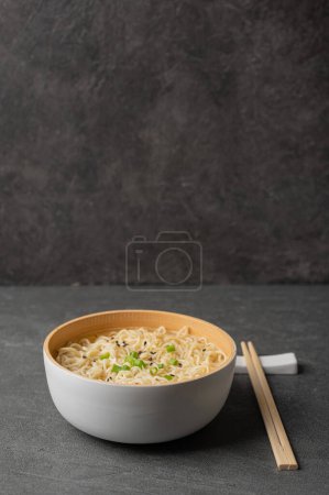 Téléchargez les photos : Assiette en bambou blanc (bol) avec nouilles aux œufs et baguettes sur fond de marbre foncé (ardoise). Asiatique traditionnel fast food - en image libre de droit