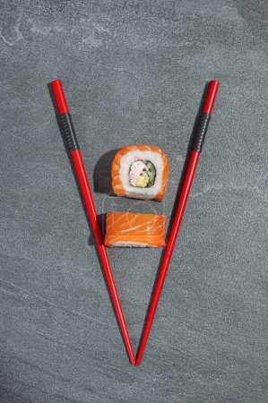 Téléchargez les photos : Rouleaux de sushi au saumon, avocat et concombre avec baguettes rouges sur fond de pierre noire (ardoise). Alimentation traditionnelle asiatique. - en image libre de droit