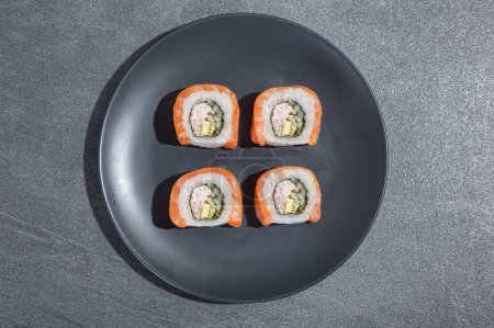 Téléchargez les photos : Les sushis roulent avec du saumon, de l'avocat et du concombre sur une assiette ronde noire sur un fond de pierre noire (ardoise). Alimentation traditionnelle asiatique. - en image libre de droit