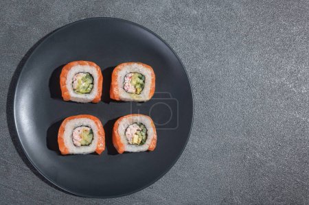 Téléchargez les photos : Les sushis roulent avec du saumon, de l'avocat et du concombre sur une assiette ronde noire sur un fond de pierre noire (ardoise). Alimentation traditionnelle asiatique. - en image libre de droit