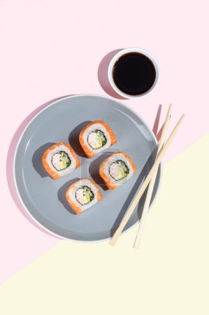 Japońskie sushi z łososiem, smocze bułki na jasnym żółto-różowym tle. Sztuka pop. Smaczne przekąski na szarym talerzu i pałeczki. Tradycyjna żywność azjatycka