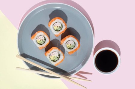 Foto de Sushi japonés con salmón, rollos de dragón sobre un fondo amarillo-rosado brillante. Arte pop. Sabrosos bocadillos en un plato gris y palillos. Comida tradicional asiática - Imagen libre de derechos