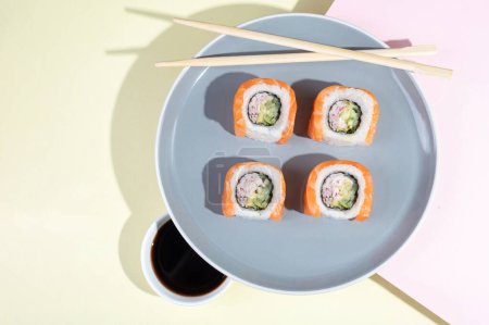 Téléchargez les photos : Sushi japonais au saumon, dragon roule sur un fond jaune-rose vif. Pop art. Snacks savoureux sur une assiette grise et baguettes. Aliments traditionnels asiatiques - en image libre de droit
