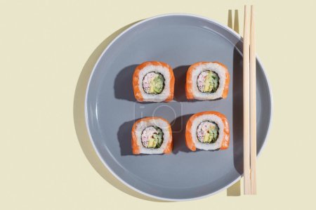 Téléchargez les photos : Sushi japonais au saumon, dragon roule sur un fond jaune vif. Pop art. Snacks savoureux sur une assiette grise et baguettes. Alimentation traditionnelle asiatique - en image libre de droit