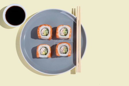 Foto de Sushi japonés con salmón, rollos de dragón sobre un fondo amarillo brillante. Arte pop. Sabrosos bocadillos en un plato gris y palillos. Comida tradicional asiática - Imagen libre de derechos