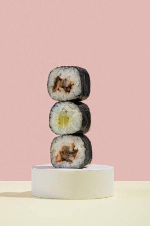 Foto de Cultura asiática, hosomaki japonés (sushi, rollos) con anguila sobre un fondo rosa y amarillo. Cocina oriental, cocina oriental. Sabrosos aperitivos en bandeja y palillos - Imagen libre de derechos