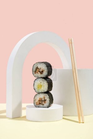 Téléchargez les photos : Culture asiatique, hosomaki japonais (sushis, petits pains) avec anguille sur fond rose et jaune. Cuisine orientale, cuisine orientale. Amuse-gueule savoureux sur plateau et baguettes - en image libre de droit