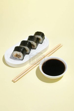 Photo for Asian culture, Japanese hosomaki (sushi, rolls) with eel on a yellow background. Oriental culinary, eastern cooking. Tasty appetizers on platter and chopsticks, soy sauce - Royalty Free Image