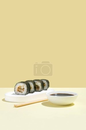 Foto de Cultura asiática, hosomaki japonés (sushi, rollos) con anguila sobre un fondo amarillo. Cocina oriental, cocina oriental. Sabrosos aperitivos en bandeja y palillos, salsa de soja - Imagen libre de derechos