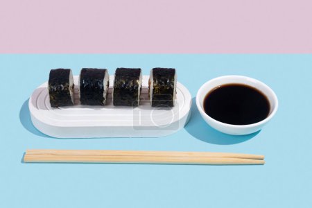 Téléchargez les photos : Hosomaki (sushi) avec anguille sur un stand blanc sur un fond uni coloré (bleu, rose). Une composition simple et concise - en image libre de droit