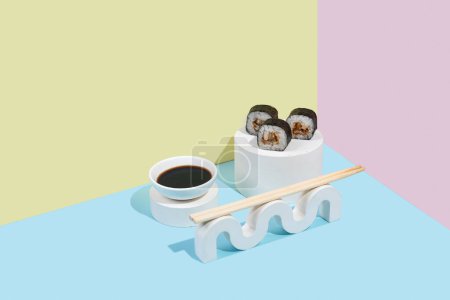 Photo for Hosomaki (sushi, rolls) with eel and soy sauce on a white plaster stand on a colorful plain background (blue, pink, yellow). A simple concise composition - Royalty Free Image