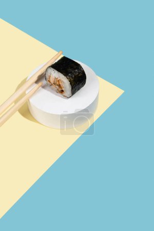 Foto de Hosomaki (sushi, rollos) con anguila sobre un soporte de yeso blanco sobre un fondo liso multicolor (azul, amarillo). Una composición simple y concisa - Imagen libre de derechos