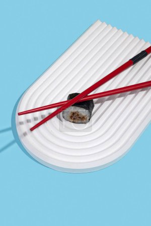 Téléchargez les photos : Hosomaki (sushis, rouleaux) avec anguille sur un support en plâtre blanc sur un fond bleu uni. Une composition simple et concise - en image libre de droit