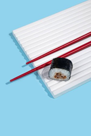 Foto de Hosomaki (sushi, rollos) con anguila sobre un soporte de yeso blanco sobre un fondo liso azul. Una composición simple y concisa - Imagen libre de derechos