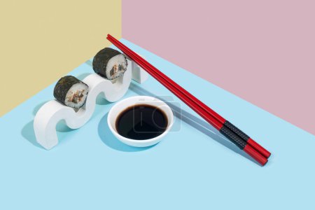 Foto de Hosomaki (sushi, rollos) con anguila y salsa de soja en un soporte de yeso blanco sobre un fondo liso colorido (azul, rosa, amarillo). Una composición simple y concisa - Imagen libre de derechos
