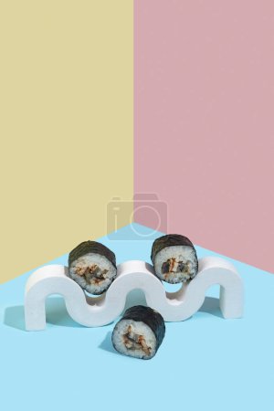 Photo for Hosomaki (sushi, rolls) with eel on a white plaster stand on a colorful plain background (blue, pink, yellow). A simple concise composition - Royalty Free Image