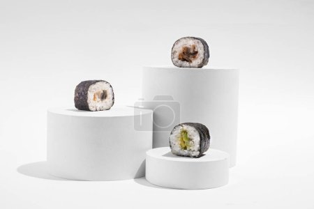 Téléchargez les photos : Hosomaki japonais (sushis, rouleaux) avec anguille sur un support en plâtre blanc sur un fond blanc uni. Une composition simple et concise - en image libre de droit