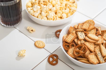 Téléchargez les photos : Homemade goodies, fast food - a bowl with popcorn, crackers and cookies on a white table. Fast food is not useful for relaxation - en image libre de droit