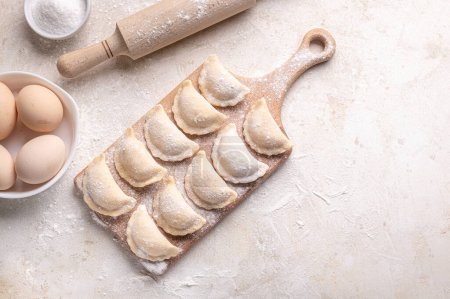 Photo for Raw dumpling with potatoes. Preparation dumplings on a light background on a wooden board. Fresh, handmade Ukrainian dumplings. National traditions, masna. Homemade dough products, craft cooking. - Royalty Free Image