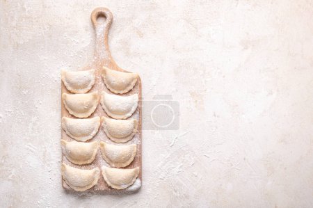Foto de Raw dumpling with potatoes. Preparation dumplings on a light background on a wooden board. Fresh, handmade Ukrainian dumplings. National traditions, masna. Homemade dough products, craft cooking. - Imagen libre de derechos
