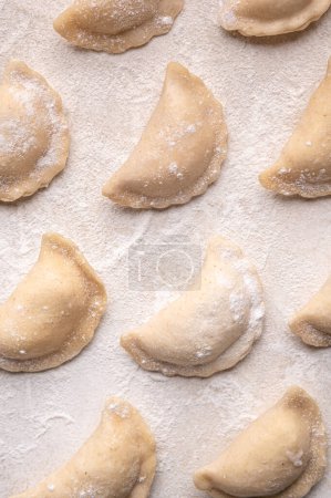 Foto de Fresh dumplings in flour on a light background. Pattern, background. Homemade craft production, national traditions, Ukrainian cuisine - Imagen libre de derechos