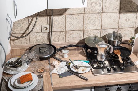 Téléchargez les photos : Cuisine désordonnée avec vaisselle sale empilée dans l'évier et sur le comptoir. Cuisine moderne avec façades blanches dans le style scandinave - en image libre de droit