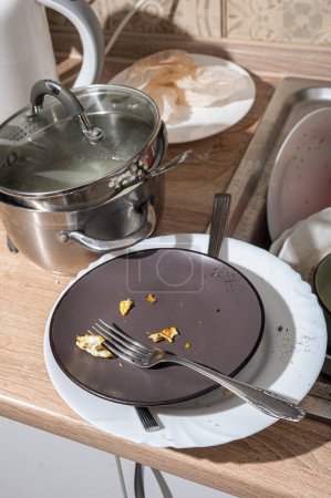 Téléchargez les photos : Cuisine désordonnée avec vaisselle sale empilée dans l'évier et sur le comptoir. Cuisine moderne avec façades blanches dans le style scandinave - en image libre de droit