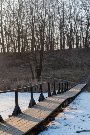 Foto de Paisaje invernal con un puente de madera que cruza un lago rodeado de juncos. La belleza serena de la naturaleza en invierno. - Imagen libre de derechos