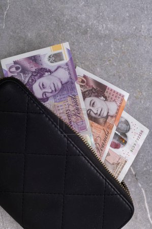 Foto de Billetera negra sobre fondo gris con billetes de 10 y 20 libras. Moneda de Gran Bretaña (Inglaterra) con un retrato de la reina Isabel - Imagen libre de derechos
