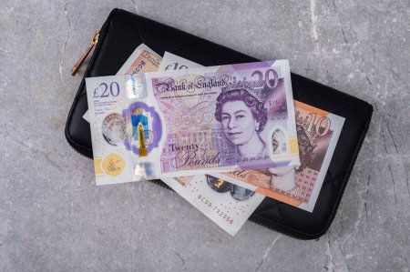 Schwarze Brieftasche auf grauem Hintergrund mit 10- und 20-Pfund-Scheinen. Währung von Großbritannien (England) mit einem Porträt von Königin Elizabeth