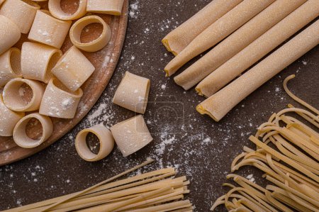 Photo for Handmade pasta on a brown background is the subject of this photo. The noodles are various shapes and sizes, and appear to be fresh and uncooked. Homemade pasta from durum wheat - Royalty Free Image