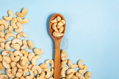 Photo for Cashew nuts in a wooden spoon on a blue background. This image represents a healthy snack option and can be used to convey concepts like nutrition, veganism, natural food, and wellness. - Royalty Free Image