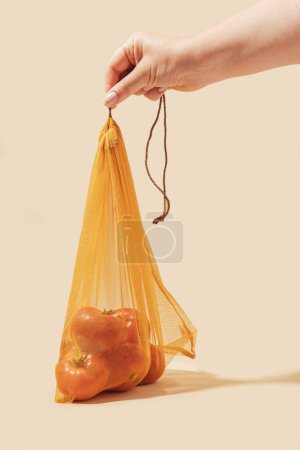 Photo for Reusable bags for buying vegetables and fruits. A woman's hand holds bags with tomatoes. Eco care, conscious consumption, care for nature. World Refueling Day - Royalty Free Image