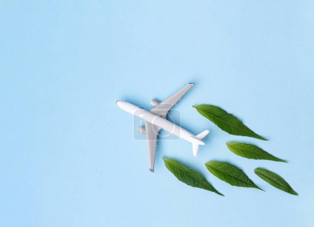 Sustainable Aviation Fuel. White airplane model, fresh green leaves on blue background. Clean and Green energy, Biofuel for aviation industry.