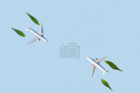 Nachhaltiger Flugkraftstoff. Weißes Flugzeugmodell, frische grüne Blätter auf blauem Hintergrund. Saubere und grüne Energie, Biokraftstoff für die Luftfahrt.