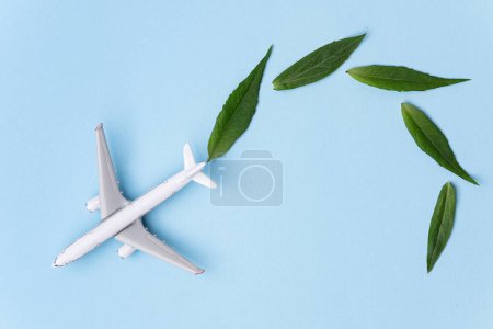Téléchargez les photos : Carburant d'aviation durable. Modèle d'avion blanc, feuilles vertes fraîches sur fond bleu. Énergie propre et verte, biocarburant pour l'industrie aéronautique. - en image libre de droit