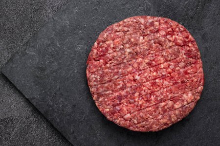 Photo for Juicy raw burger patty against a dark backdrop. Creation is perfect for burger lovers seeking an authentic and flavorful experience - Royalty Free Image