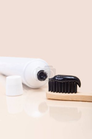Foto de Tubo blanco con pasta de dientes negra y cepillo de bambú con cerdas negras sobre fondo beige. Minimalismo. Atención de la salud dental - Imagen libre de derechos