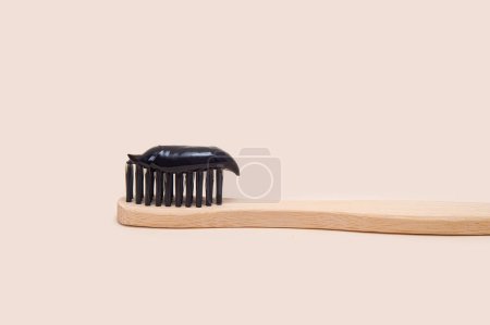 Téléchargez les photos : Dentifrice noir sur une brosse en bambou à poils noirs sur fond beige. Minimalisme. Soins dentaires - en image libre de droit