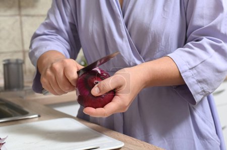 Photo for A woman peels red onions in her kitchen. Female hands hold a salad onion - Royalty Free Image
