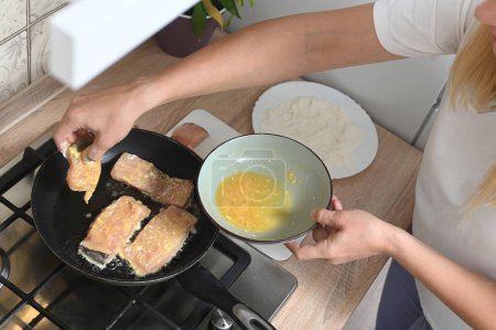 Téléchargez les photos : Women's hands fry pieces of fish in a batter - flour and eggs. Home cooking, simple light dishes - en image libre de droit